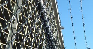 Aprison fence with barbed wire is picture in front of a bright blue sky