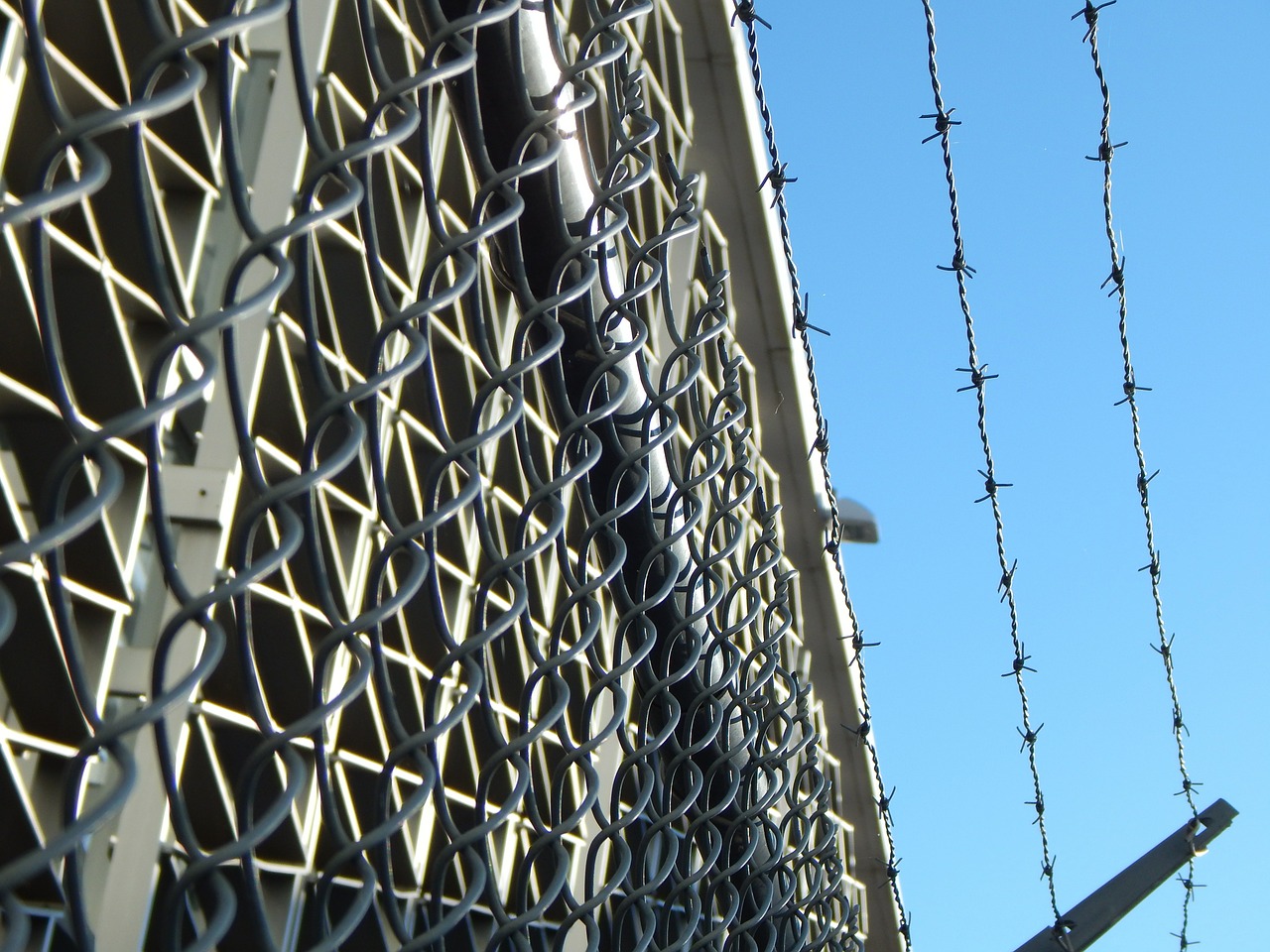 Aprison fence with barbed wire is picture in front of a bright blue sky