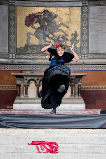 Dancer wearing black clothing, lifting their arms and one leg
