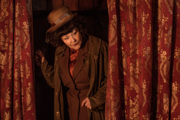 Photo of Frances Barber as Mrs. Ambrigail peeking through a curtain