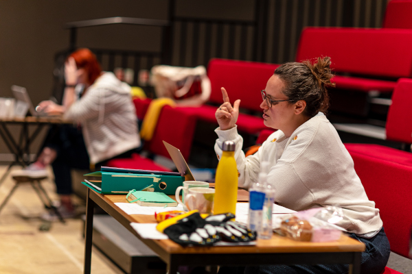 Photo of director Helen Eastman sitting at a table and speaking during rehearsal