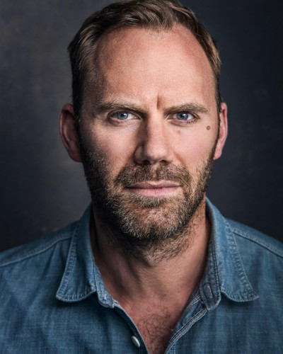 Will Thorp wearing a blue shirt and looking into the camera intently