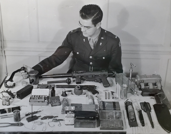 Photo of man sitting at a table with World War II weapons