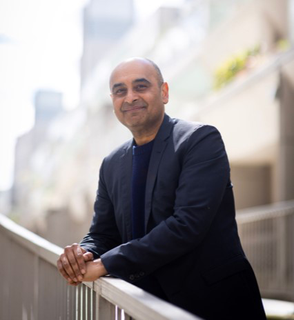 Photo of Suk Pannu, creator of 'Mrs Sidhu Investigates', standing at a balcony and smiling