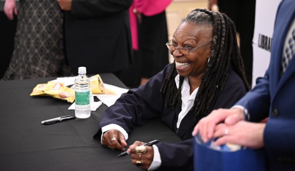 Photo of Whoopi Goldberg smiling at a book signing table