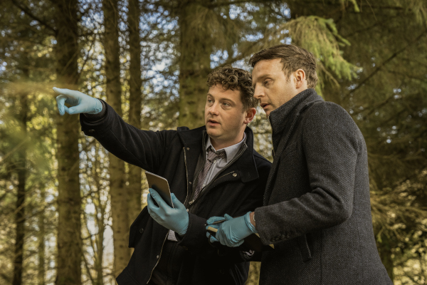 Two men standing in the woods with one man pointing into the distance