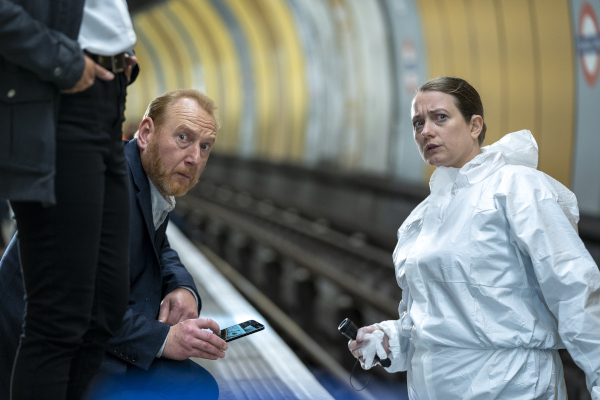 A man and woman in the London tube station, looking toward the camera